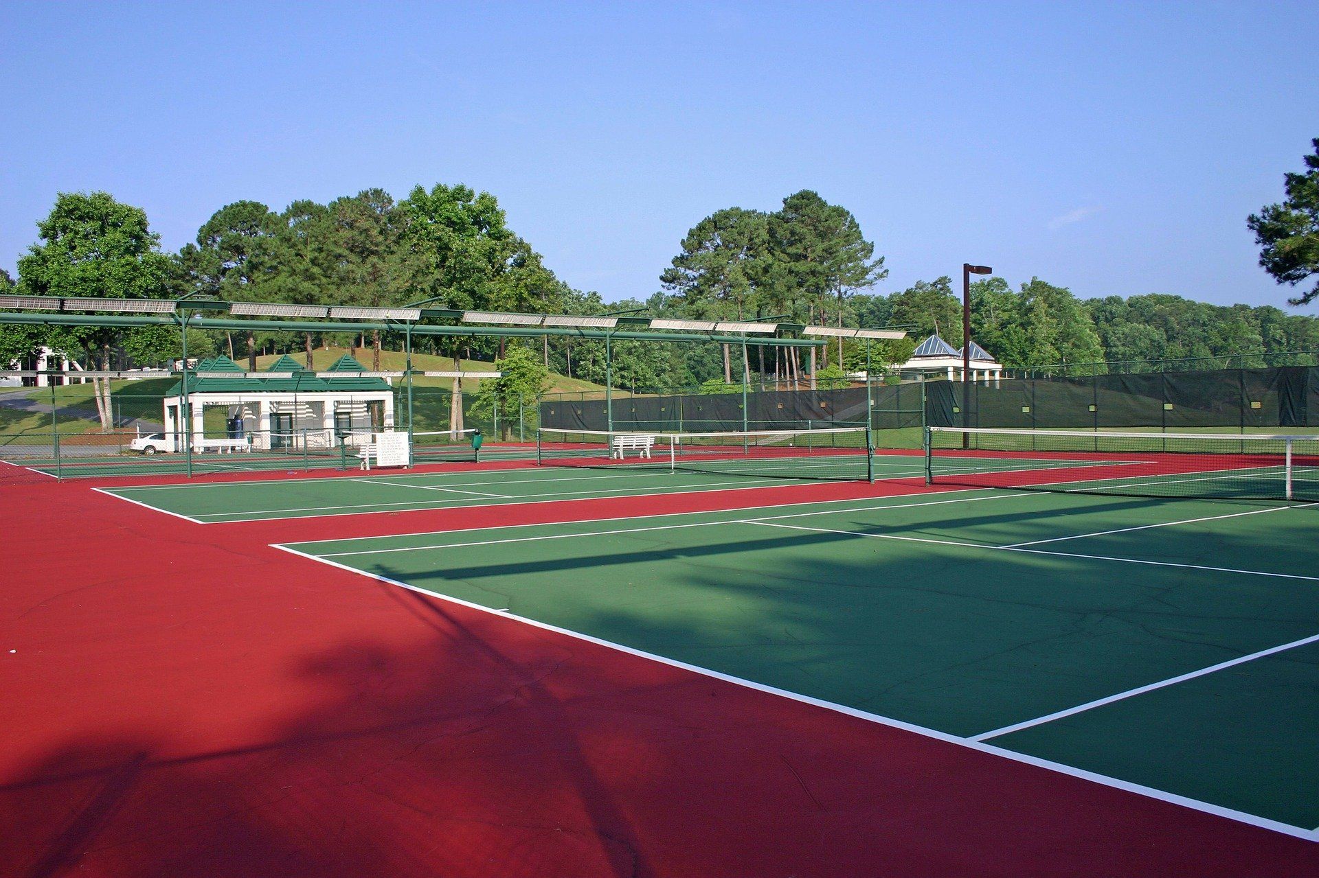 An empty tennis court bathed in sunlight, with green and red colors contrasting on the playing surface, ready for a match.