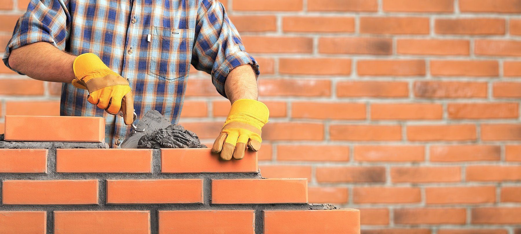 Skilled bricklayer meticulously applying brick masonry to an exterior wall using a trowel and putty knife.