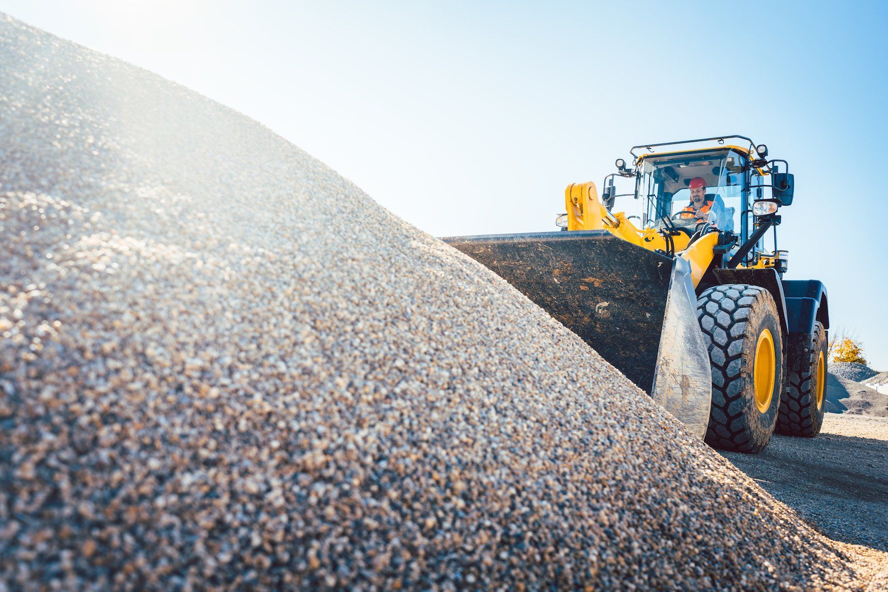 A gravel delivery truck unloading a pile of small, gray gravel onto a driveway.