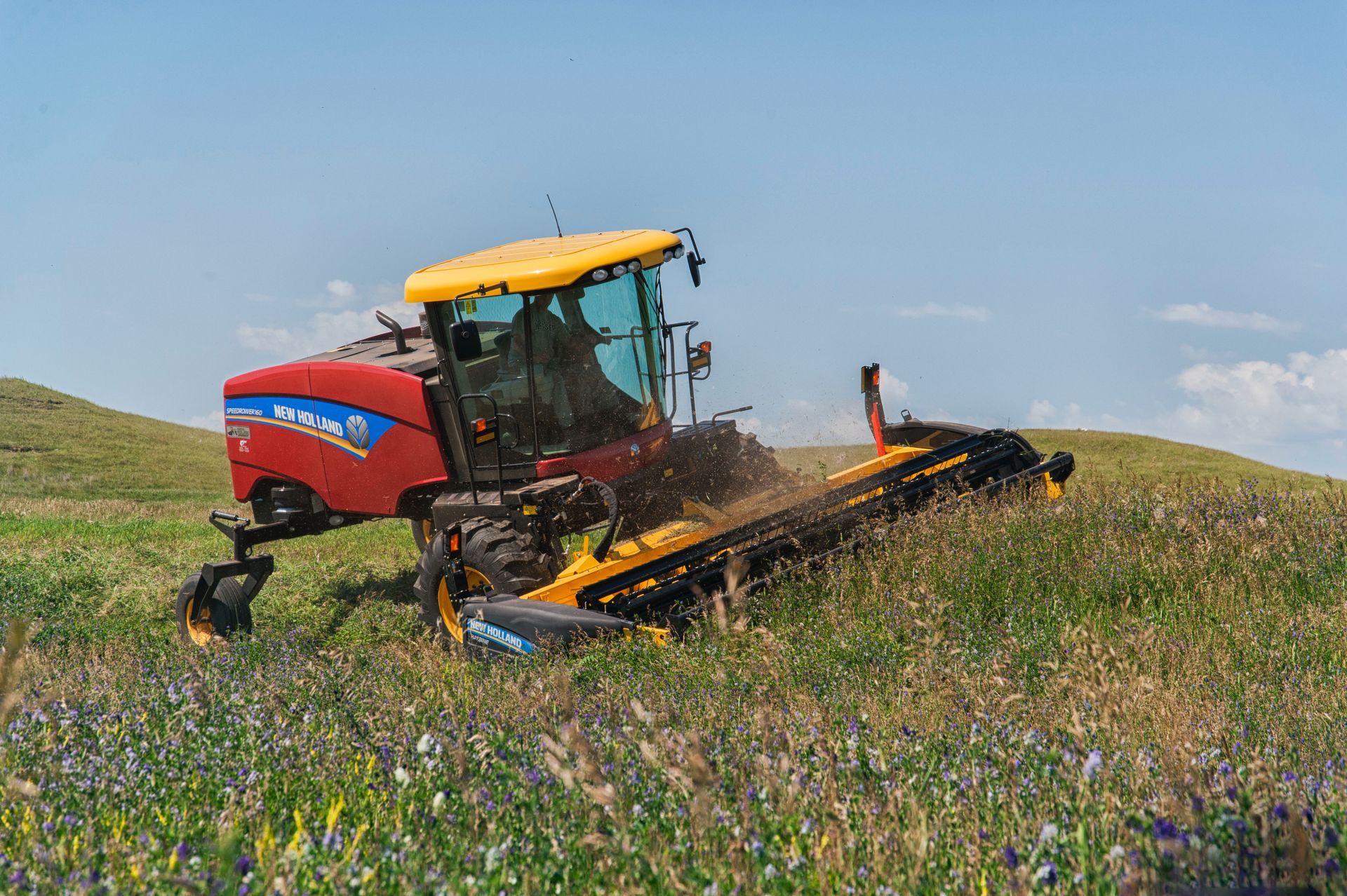 Red tractor plowing a lush green field on a sunny day.
