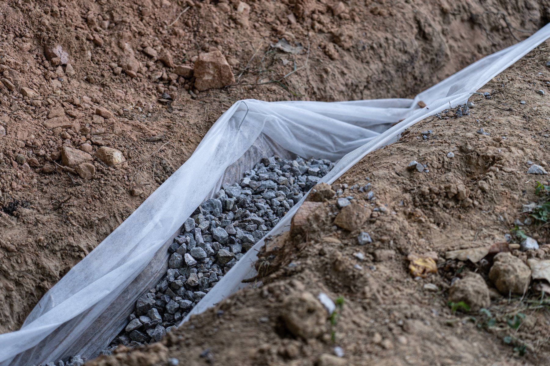 Drainage rock neatly laid within a French drain, a crucial component of a home's drainage system to alleviate water issues and prevent flooding.