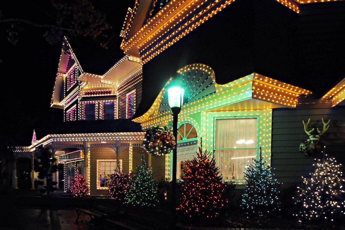 Colorful Christmas lights adorn the exterior of a house and illuminate nearby trees, creating a festive and magical atmosphere.