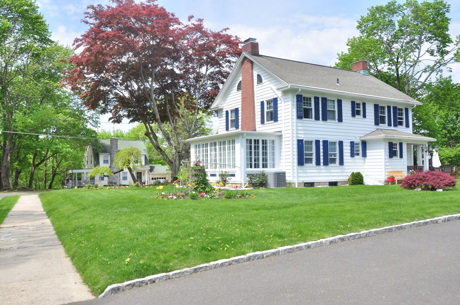 Stunning home featuring white siding, elegant royal blue window shutters, and a lush green grass lawn.