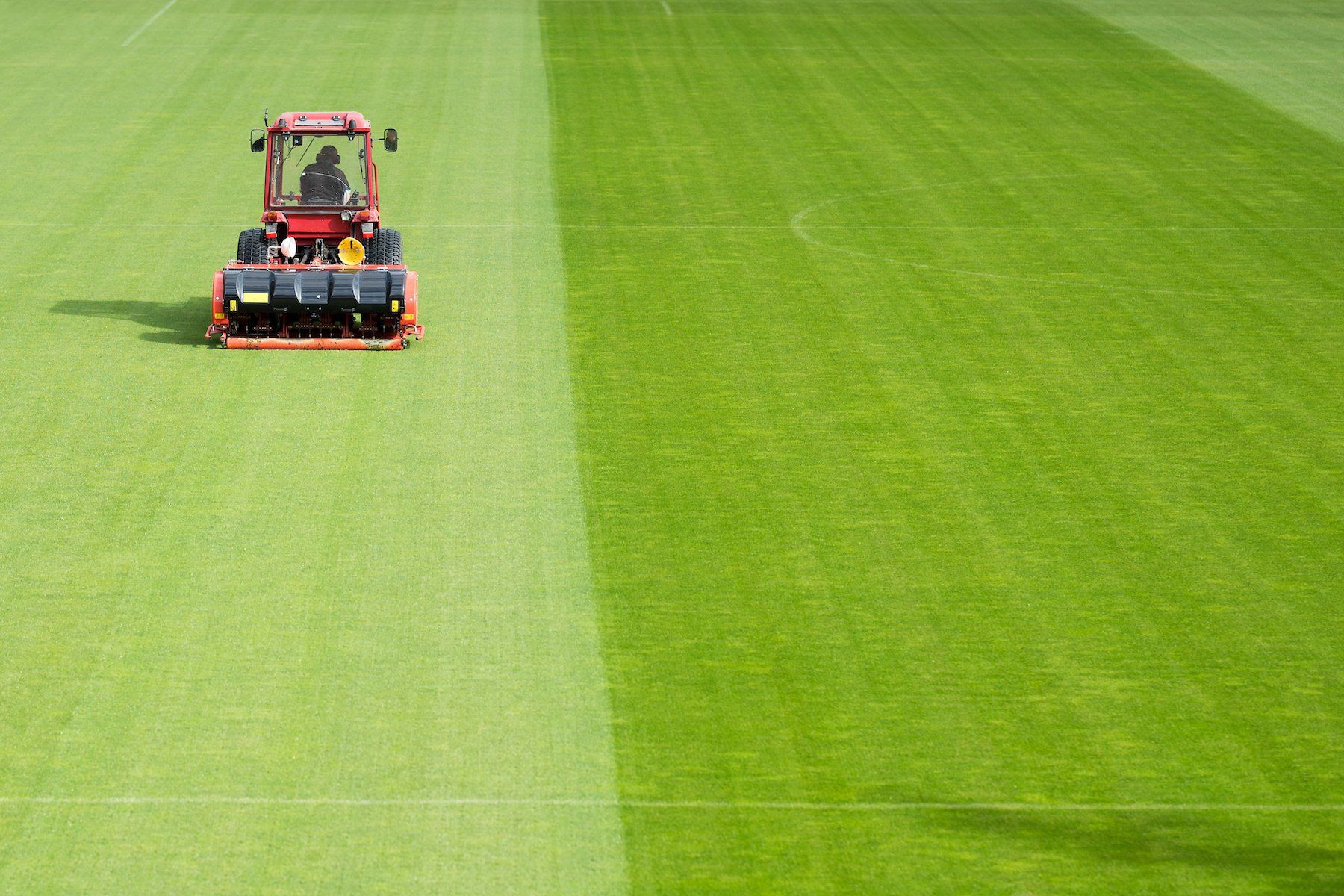 Man operating a tractor with aeration equipment on a soccer field.