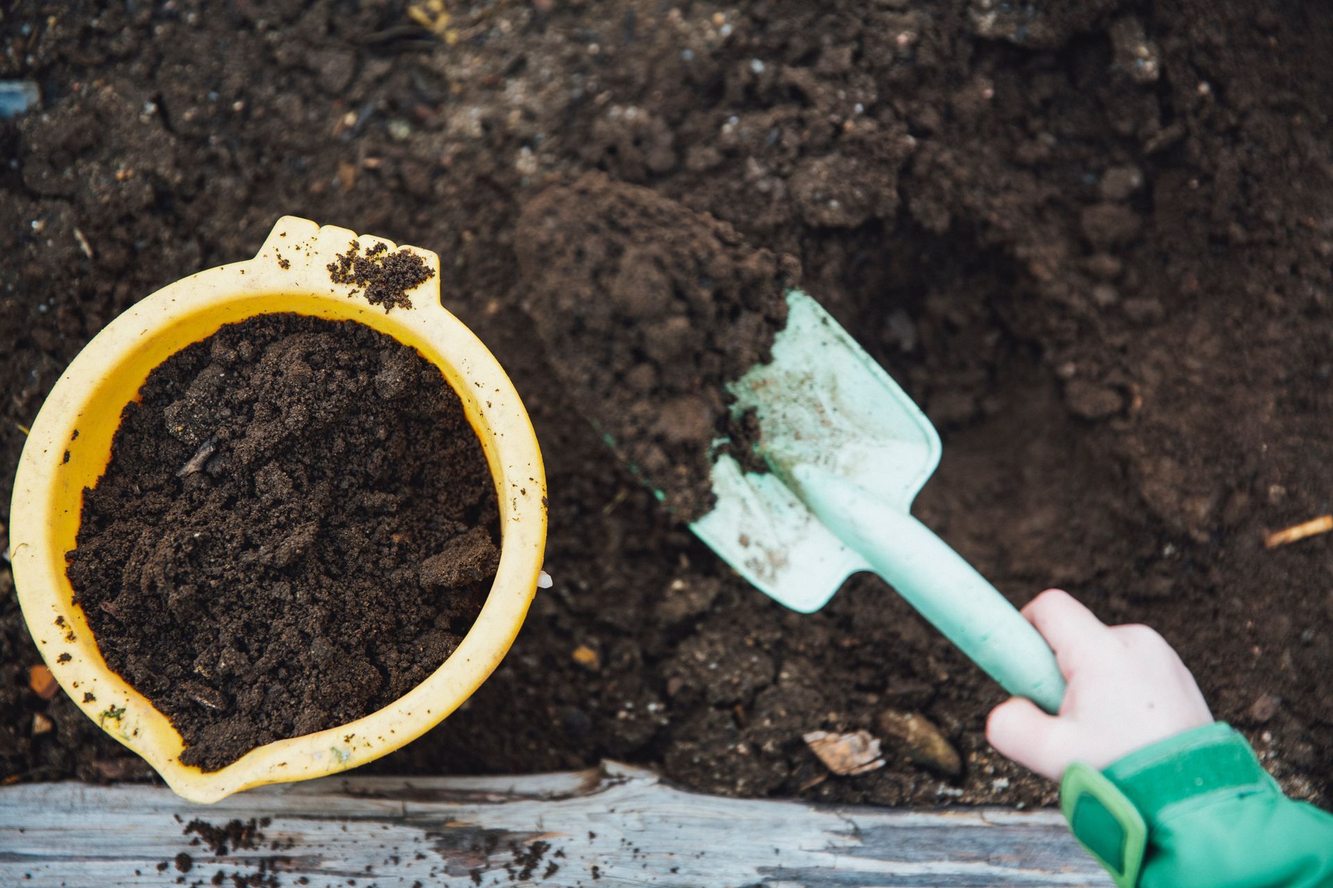 Person using a hand shovel to carefully turn and aerate organic compost in a garden bed.