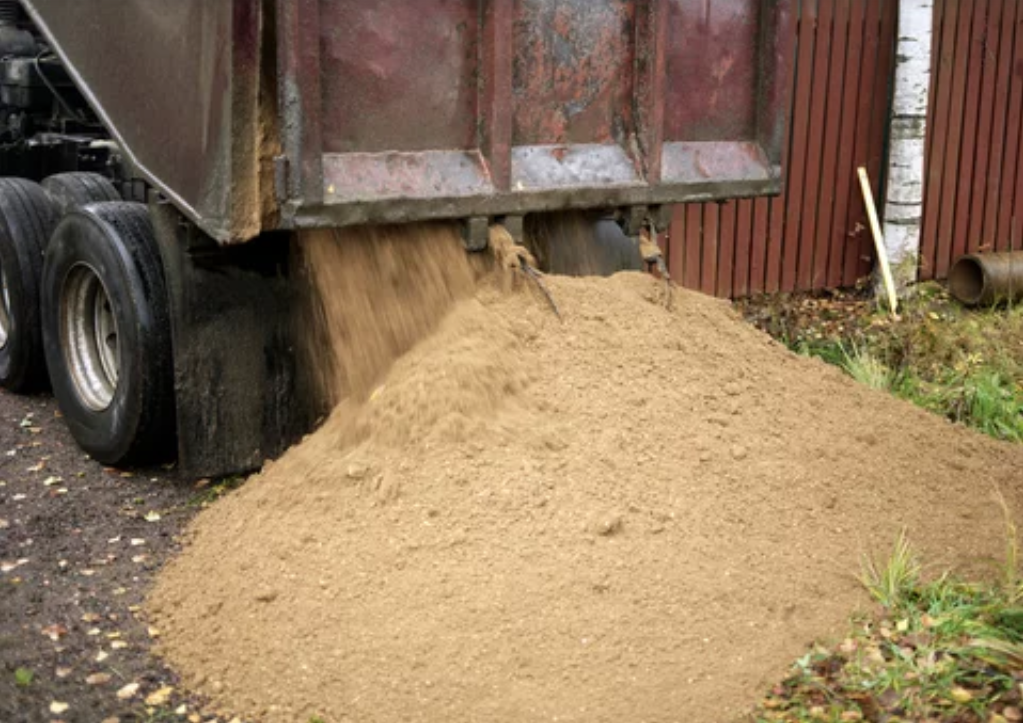 Large dumper truck offloading a load of sand onto a construction site.