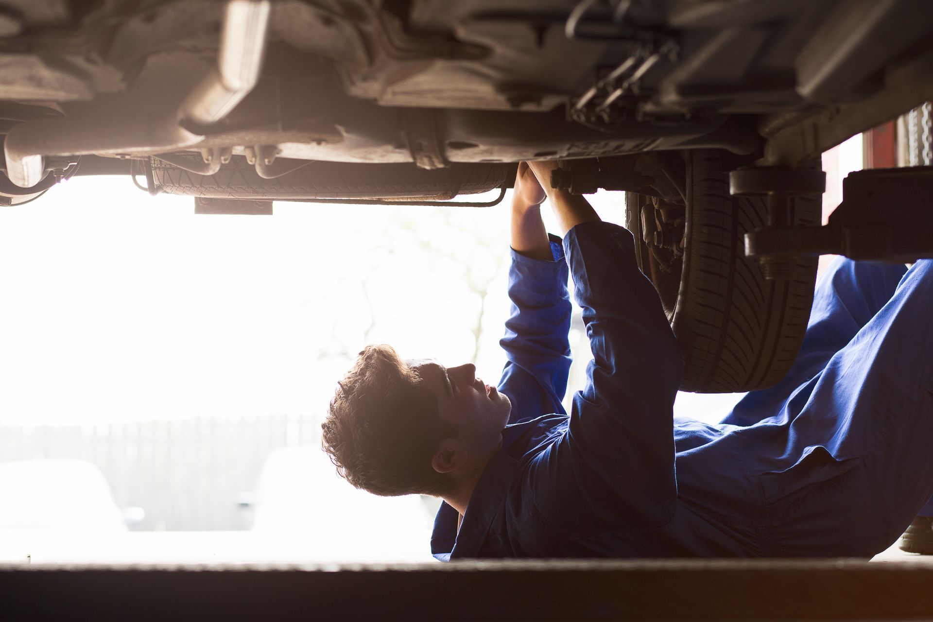 A mechanic is working under a car in a garage.