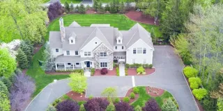 An aerial view of a large house with a large driveway surrounded by trees.