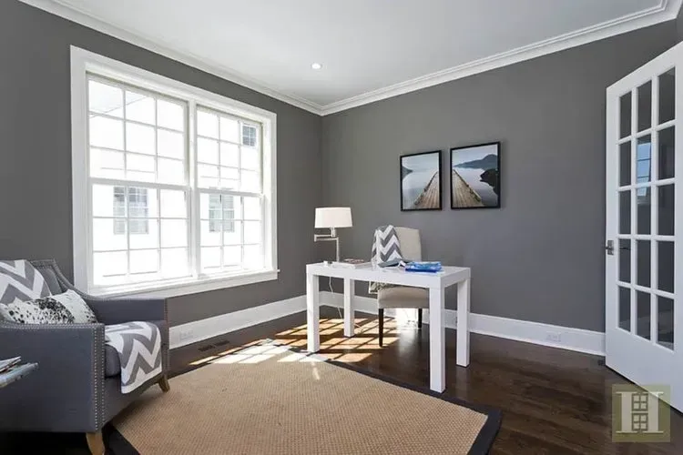 A living room with a desk , chair , rug and large windows.