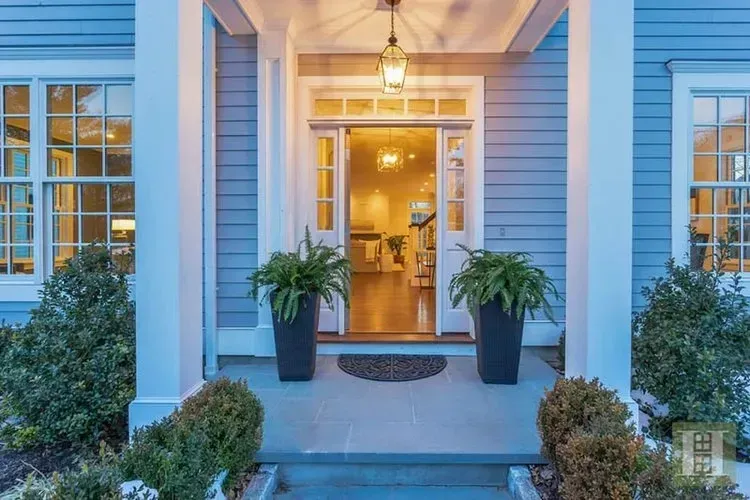 The front door of a house is open and there are two potted plants in front of it.