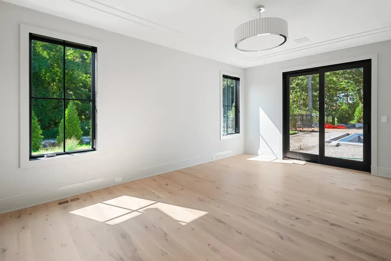 An empty living room with hardwood floors and two windows.