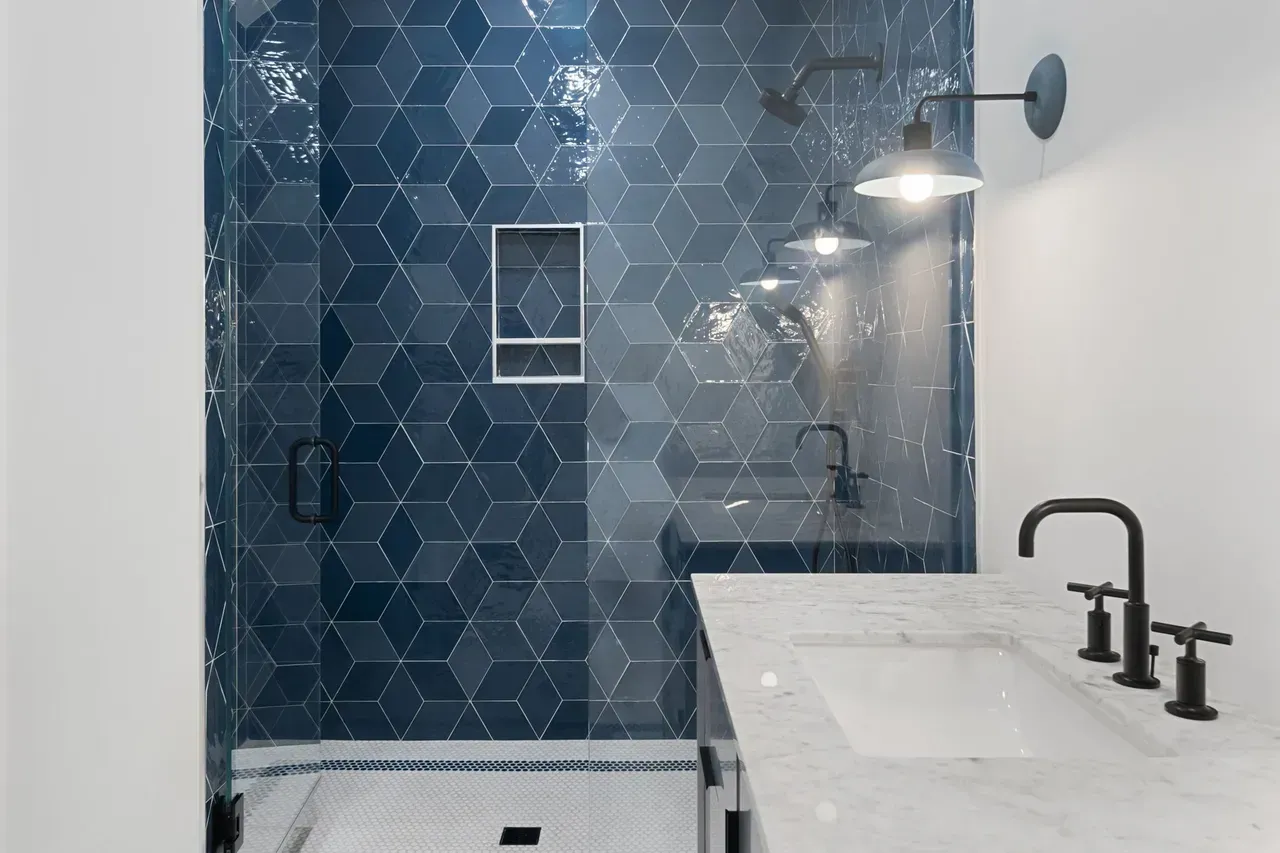 A bathroom with blue tiles , a sink , and a shower.