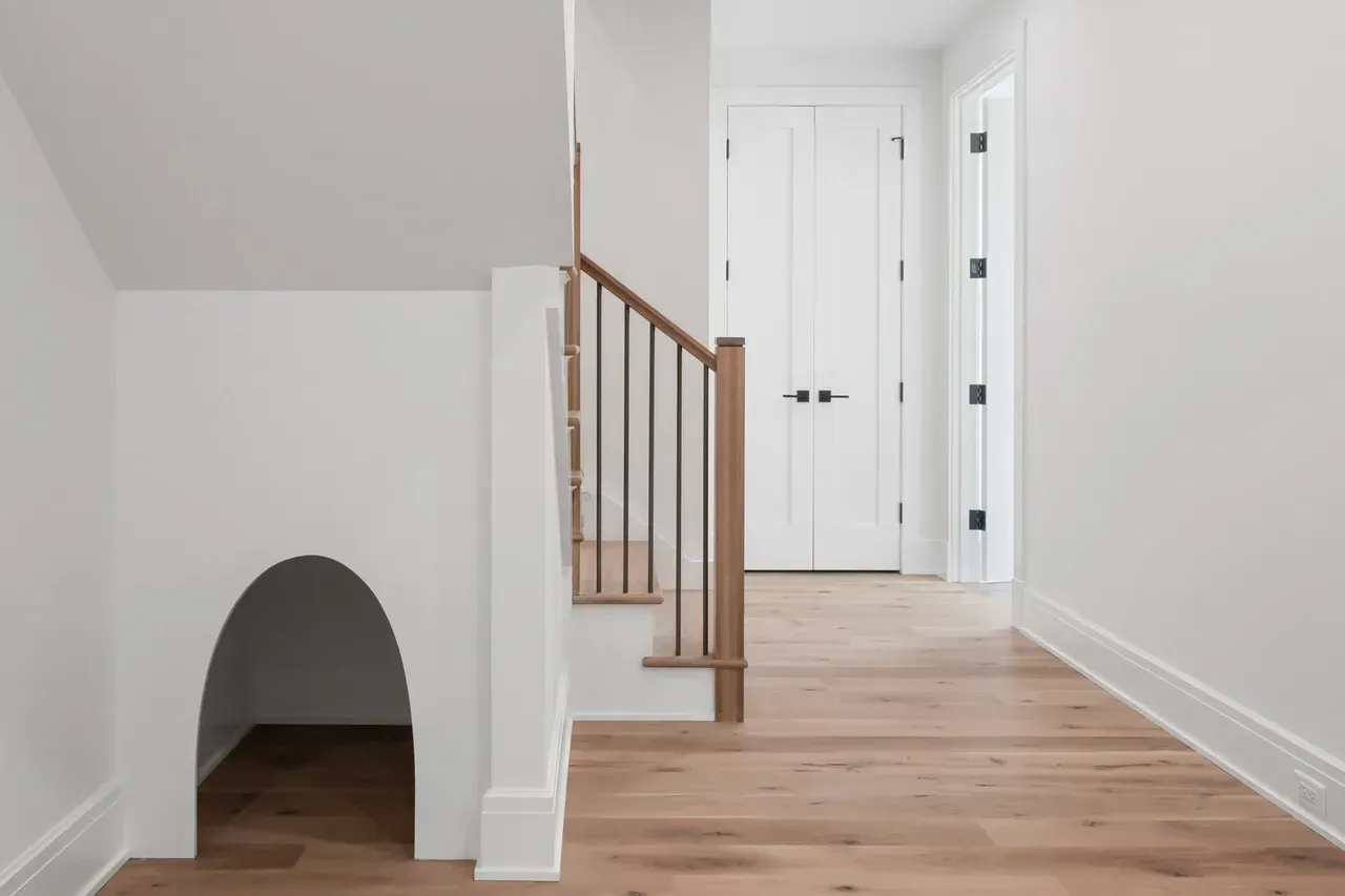 A hallway with wooden floors and stairs in a house.