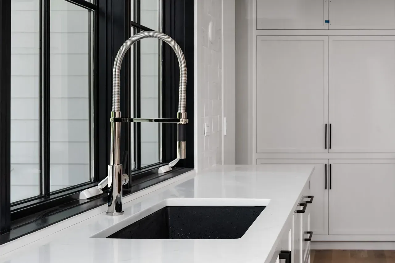 A kitchen sink with a faucet and a window in the background.