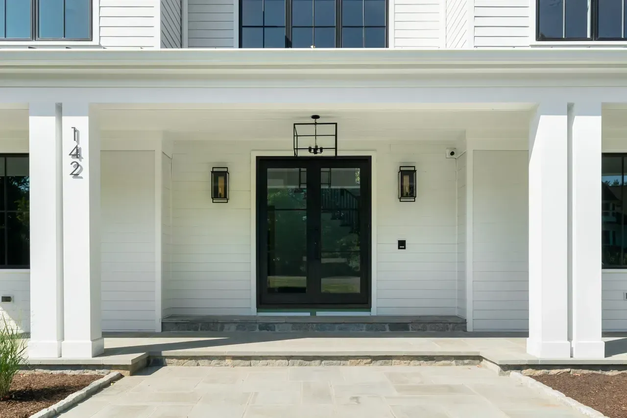 The front of a white house with black doors and a porch.