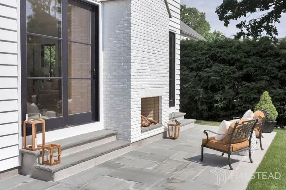 A patio with a fireplace and chairs in front of a white brick house.