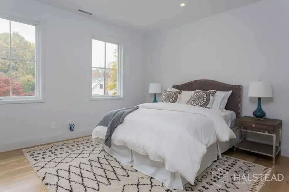 A bedroom with a bed , two lamps , a rug and two windows.