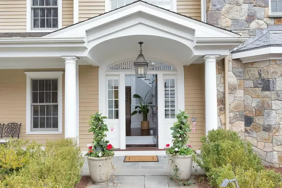 The front door of a house with a porch and potted plants.
