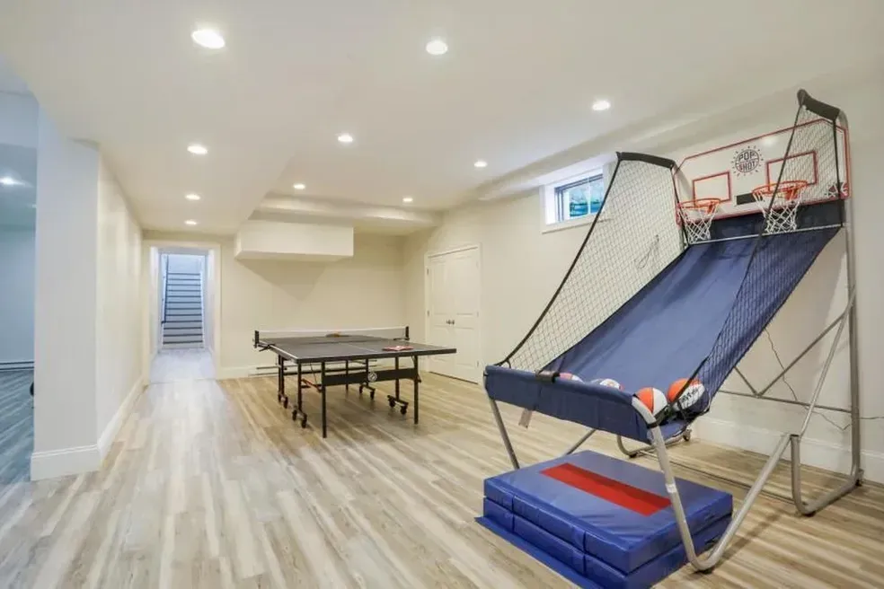 A basement with a ping pong table and a basketball hoop.