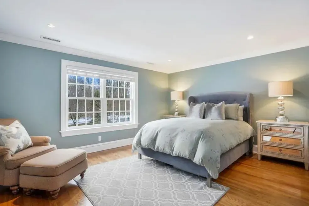 A bedroom with a bed , chair , nightstand and window.