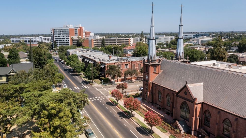 Aerial view of a city street with a church featuring two tall steeples and surrounding buildings.