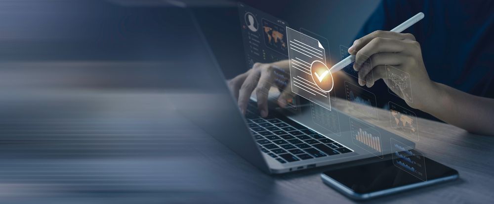 A person uses a stylus on a digital interface above a laptop to select a checkmark icon, symbolizing document approval.