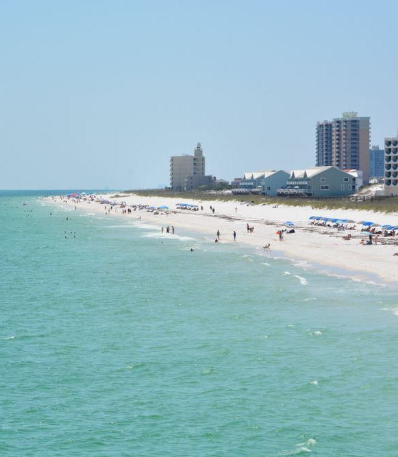 Beach with turquoise water, white sand, people, and buildings under a clear blue sky.