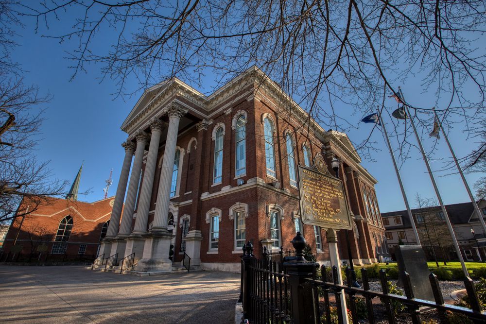 Brick building with white columns, blue sky, and bare tree branches.
