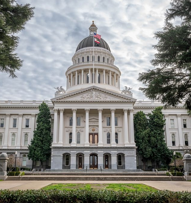 California State Capitol building with a large dome, columns, and flag, in Sacramento.