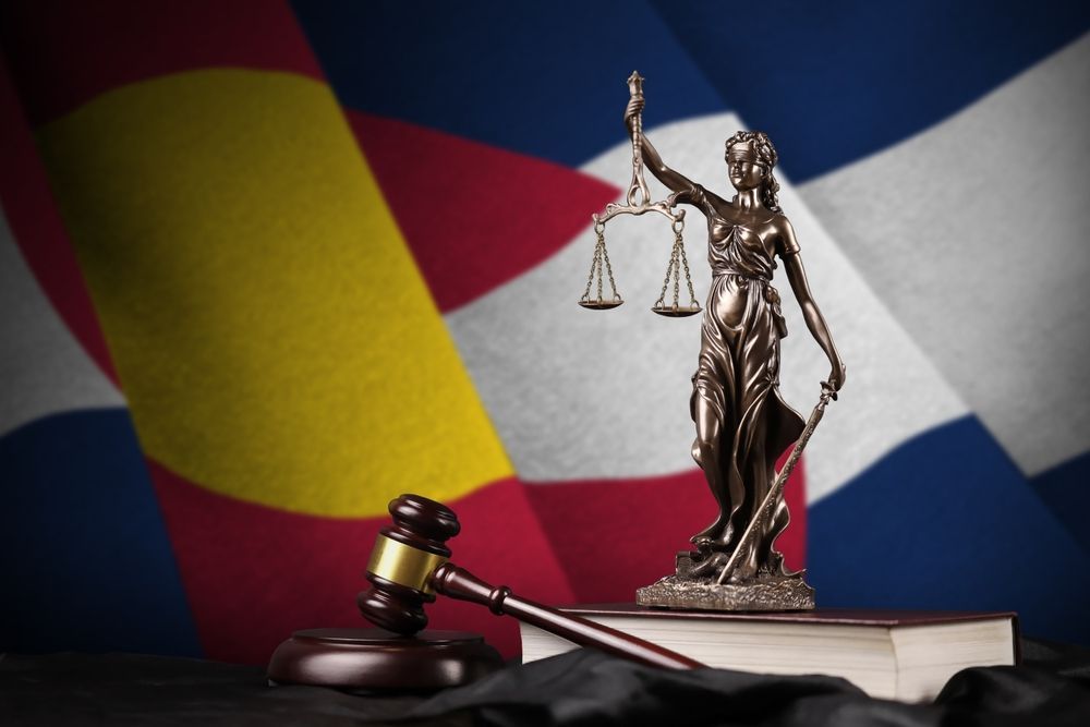 A statue of justice sitting on top of a book in front of the Colorado flag