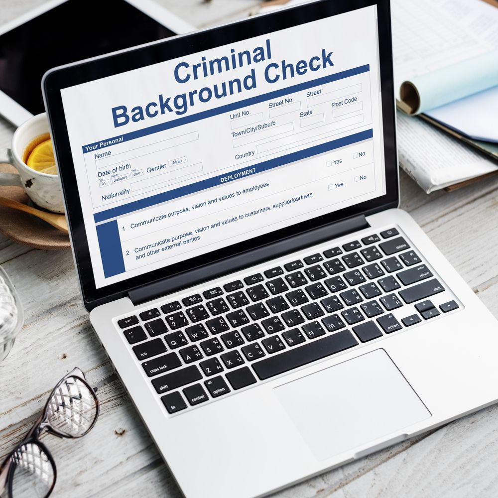 Laptop displaying a criminal background check form on a desk with glasses and a cup of tea.