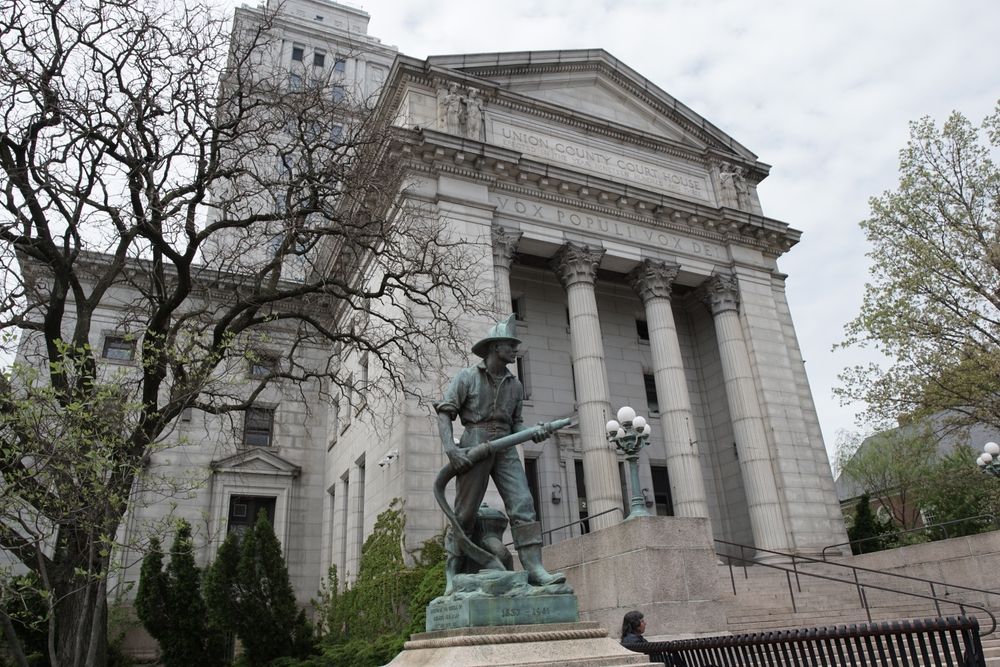 Statue of a man with a hose in front of a large, classical building with columns.