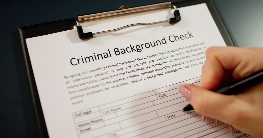 Laptop displaying a criminal background check form on a desk with glasses and a cup of tea.