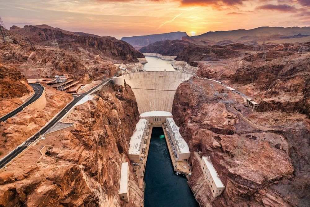 Aerial view of the Hoover Dam nestled in a rocky canyon during a golden sunset.