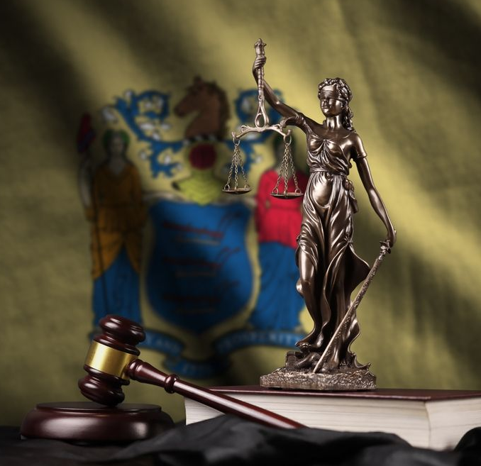 Lady Justice statue with gavel and books in front of New Jersey flag.