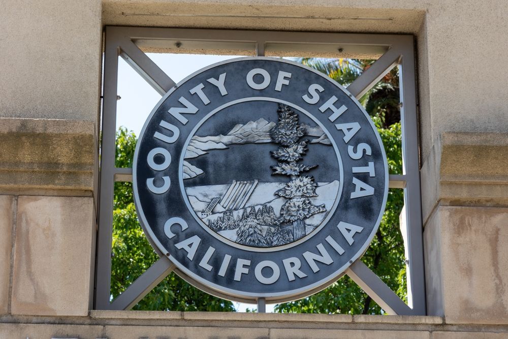County of Shasta, California emblem in a metal frame; outdoor setting with trees visible.