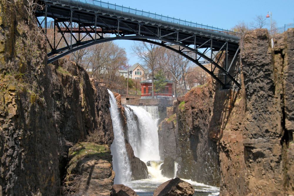 Waterfall cascading under a black metal bridge; brown cliffs surround the water.