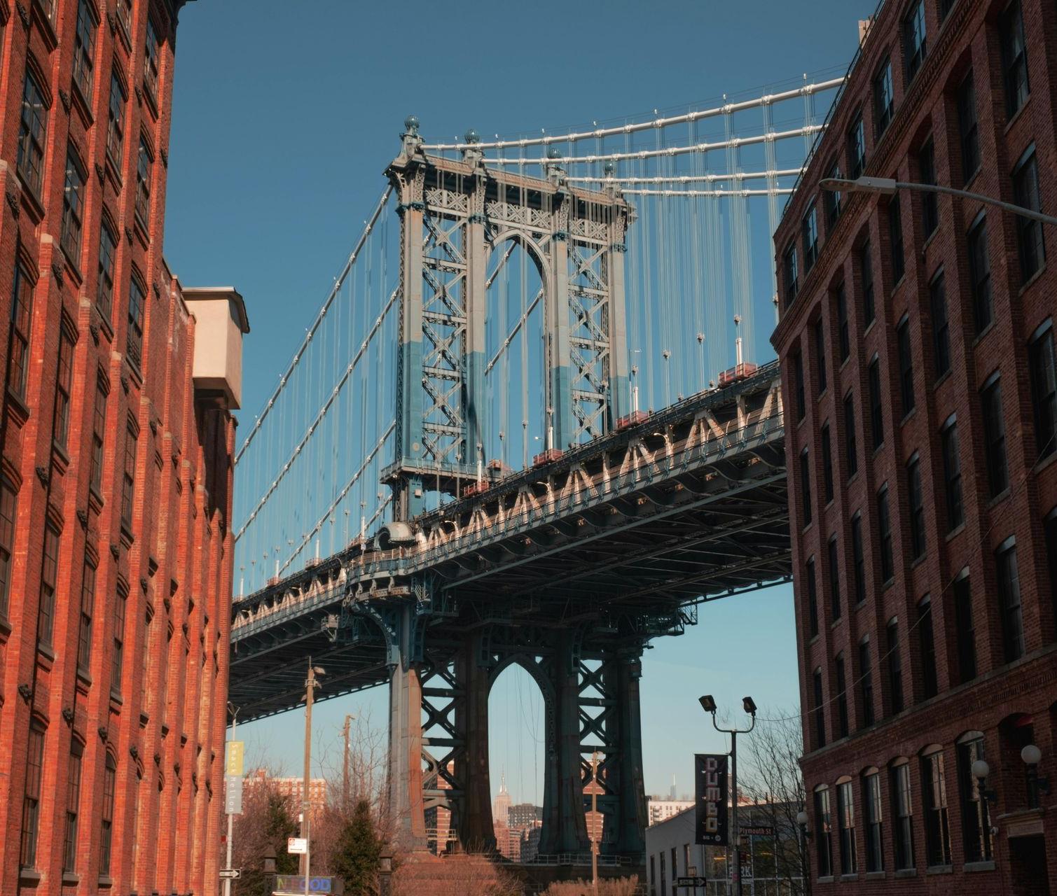 Manhattan Bridge viewed from between two brick buildings on a sunny day.