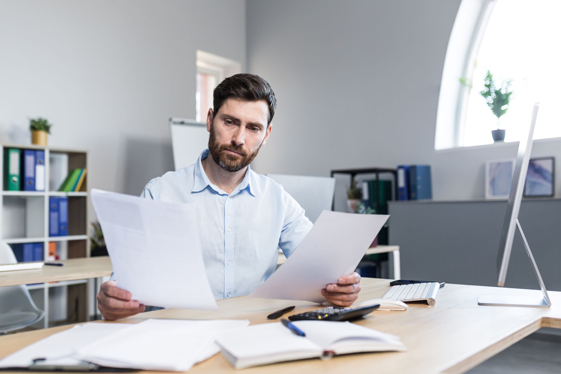 A man is sitting at a desk in an office looking at papers trying to identify a fake degree certificate