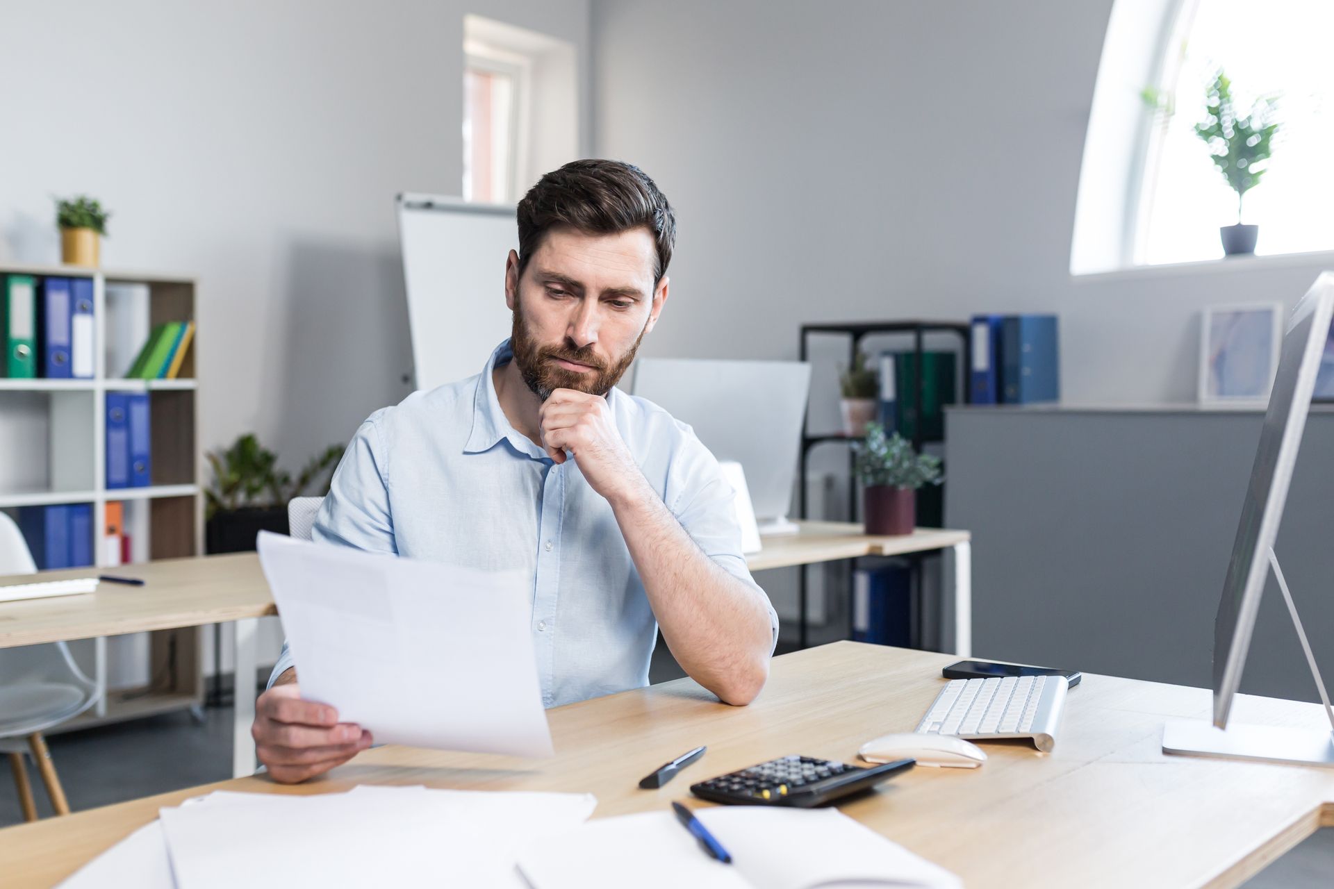 A man is sitting at a desk in an office looking at a fake degree certificate