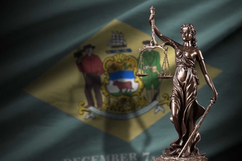 A statue of lady justice stands in front of the flag of delaware