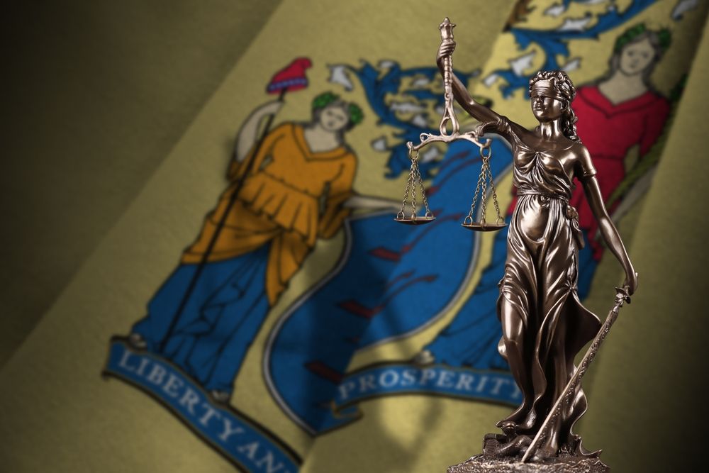 A statue of lady justice stands in front of a new jersey state flag