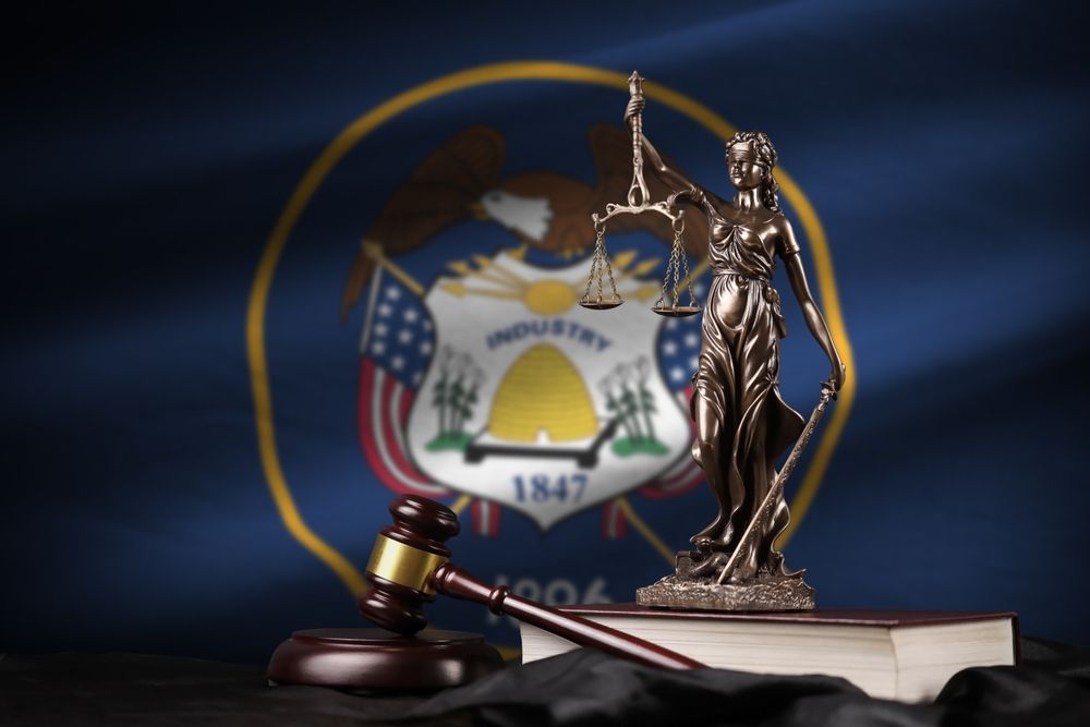 A statue of justice sitting on top of a book with the utah flag in the background