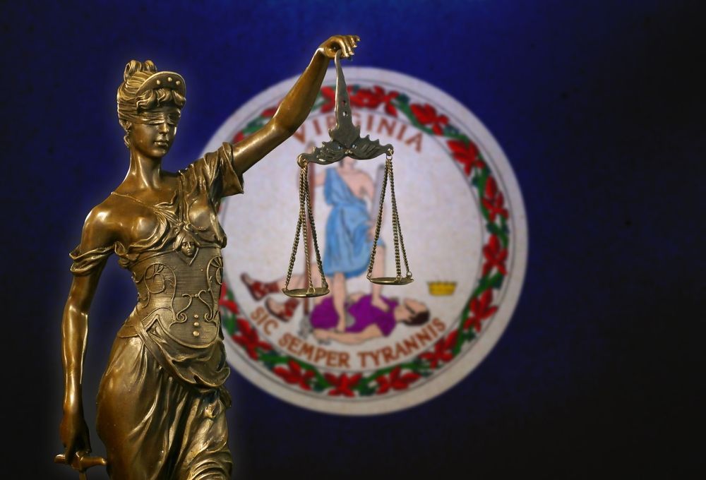 A statue of lady justice holding scales in front of a virginia state seal