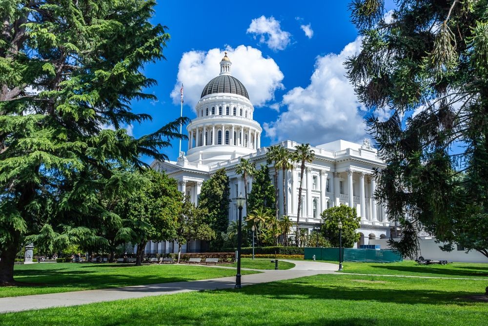 The capitol building is surrounded by trees and grass on a sunny day.