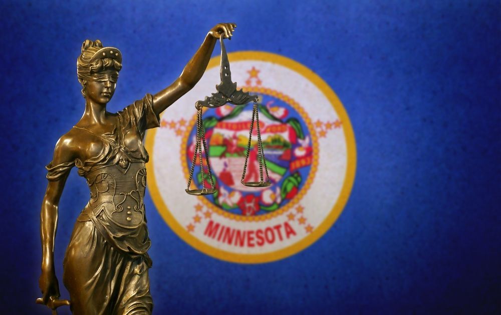 A statue of justice in front of a minnesota flag