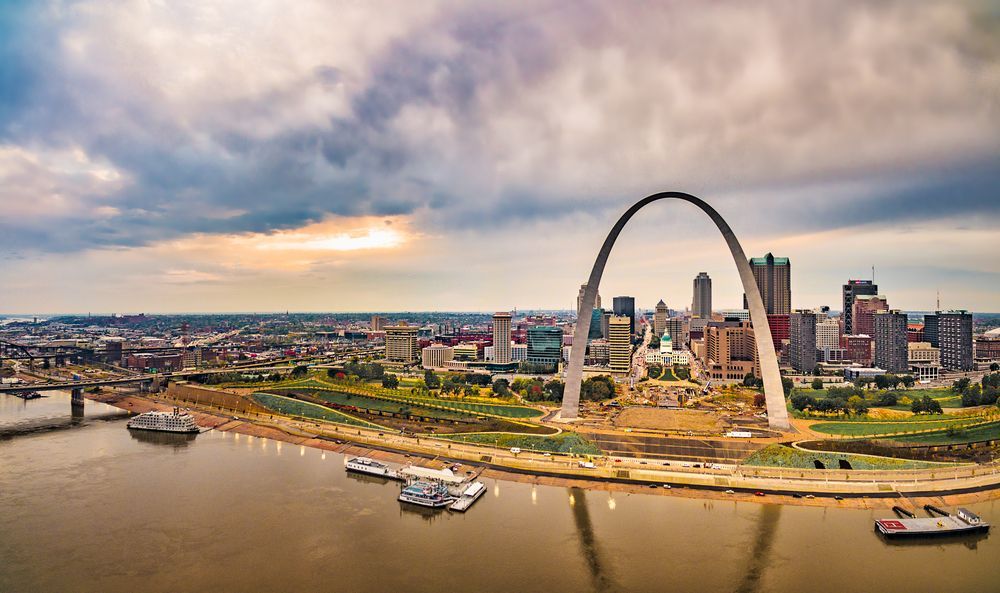 The Gateway Arch in St. Louis overlooking the city, river, and cloudy sky.