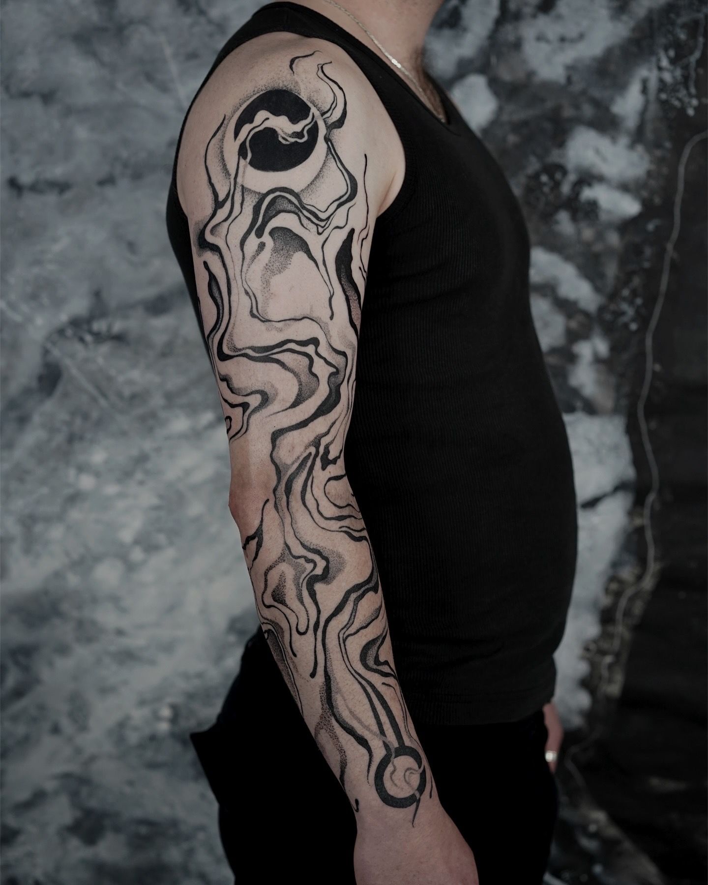Man with a full sleeve tattoo of swirling black ink and a dark circular design on his shoulder.