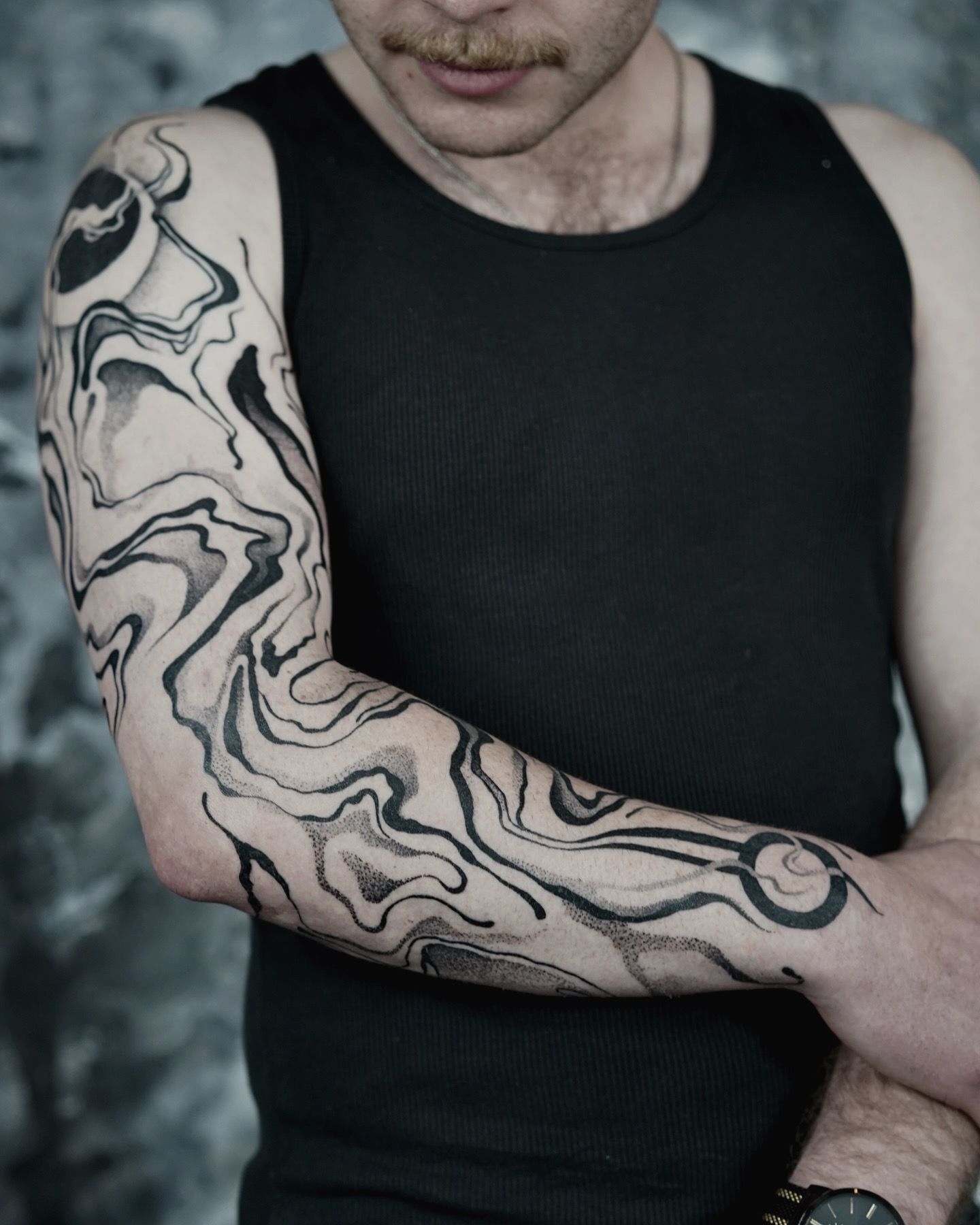 Man with abstract black and gray arm sleeve tattoo, wearing a black tank top.