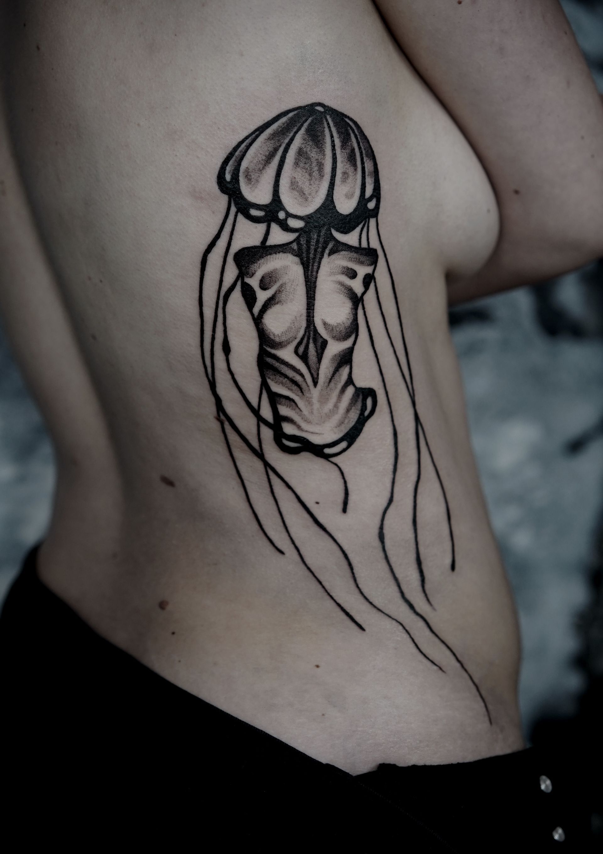 Black jellyfish tattoo on a person's side, ribs, and torso.